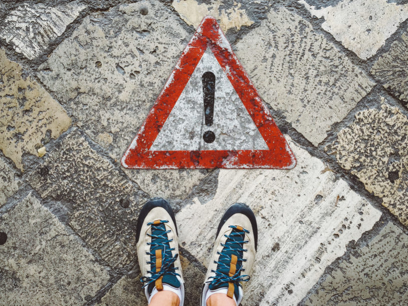 A pair of feet standing on a wet stone walkway. A warning sign lies on the ground.